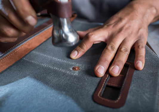 Hammer pounding in copper rivet on leather bag